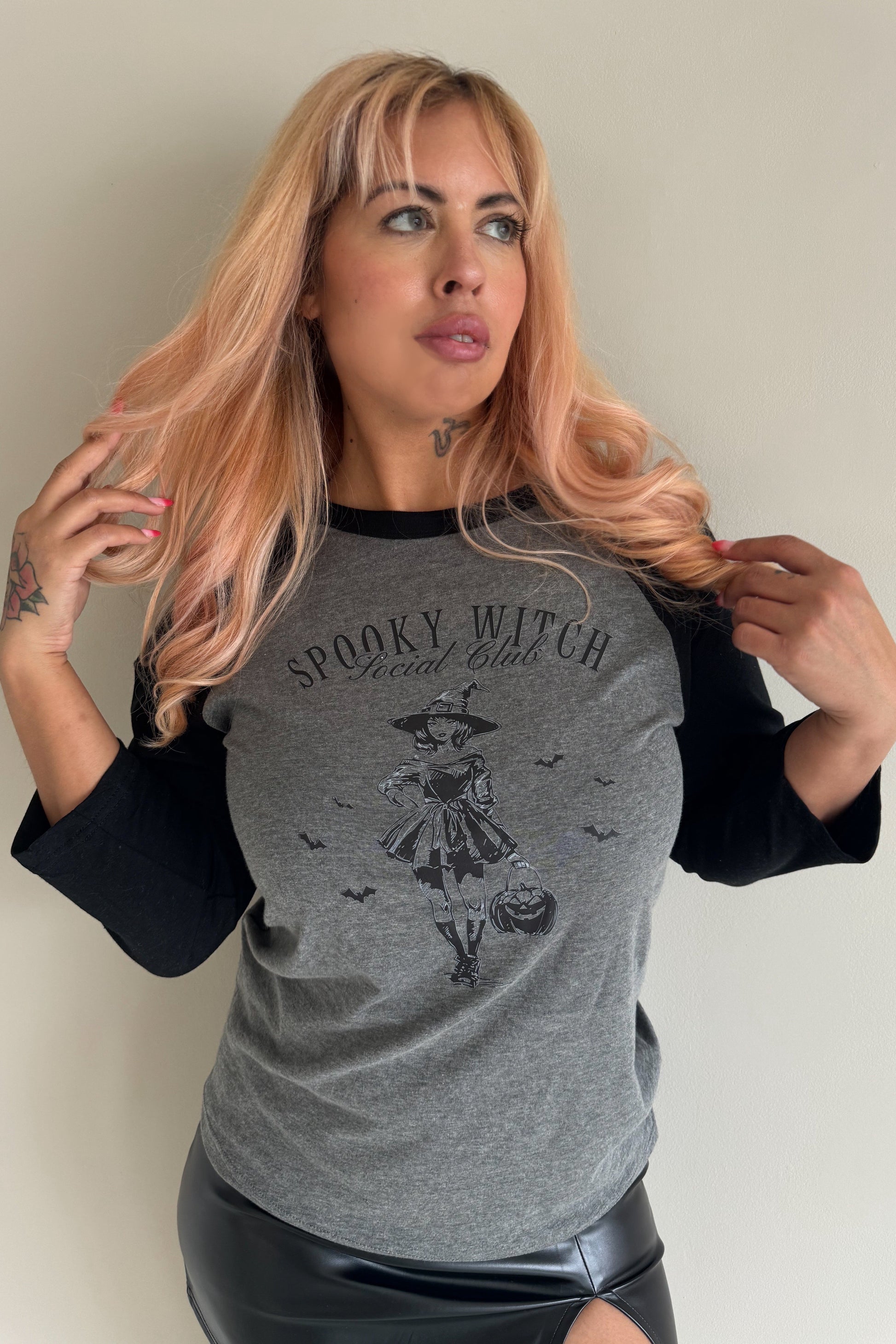 A woman wearing a 3/4 sleeve baseball t-shirt with 'Spooky Witch' text and an illustration of a witch on it.