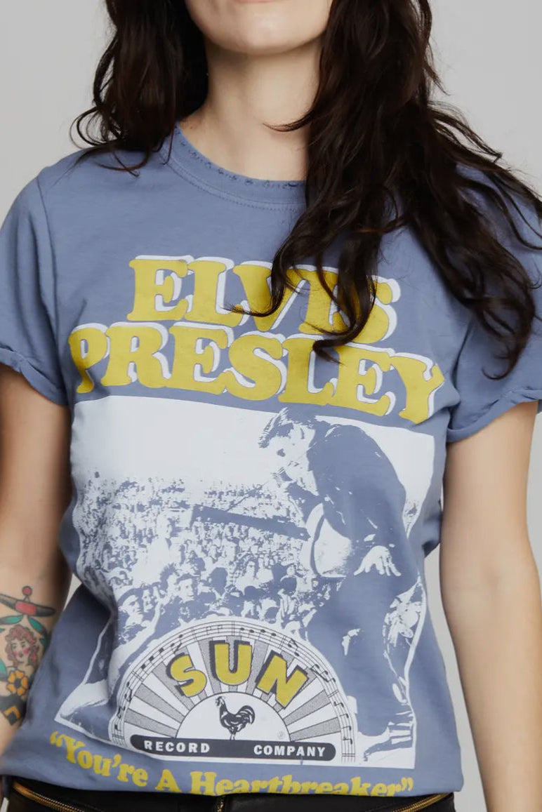 A woman wearing a blue t-shirt with 'ELVIS PRESLEY' and 'SUN RECORDS' text, along with the song 'You're a Heartbreaker'.