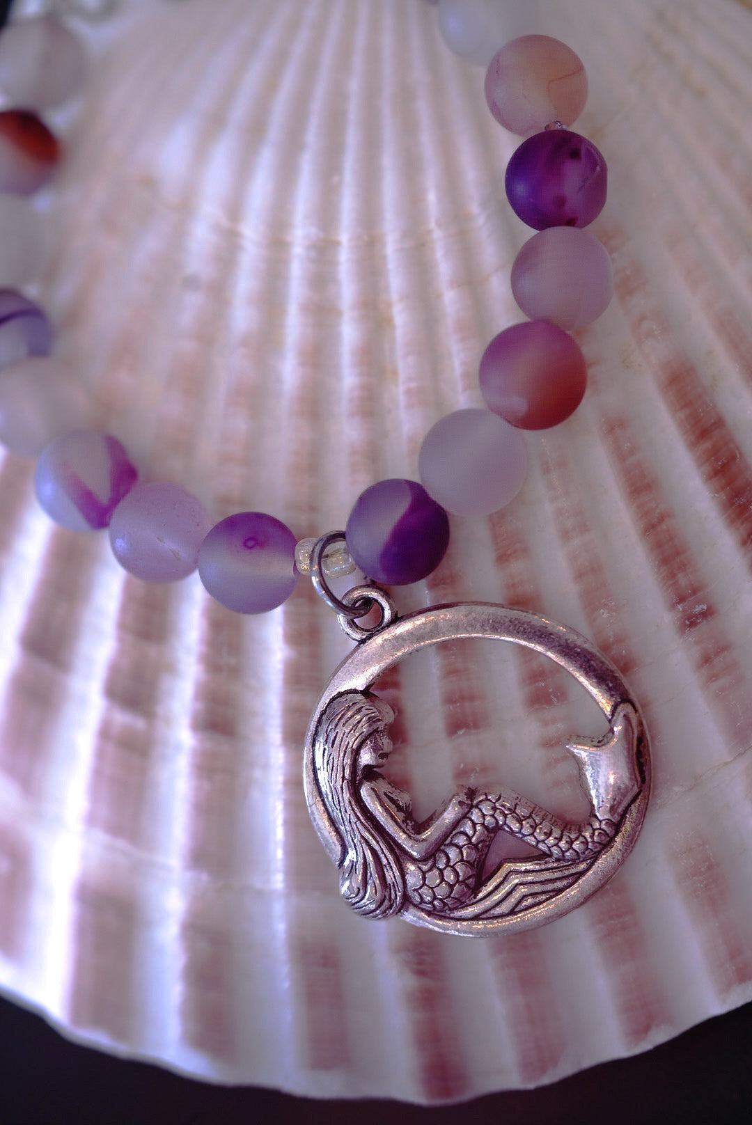 Bracelet with mermaid charm and multicolored beads on a shell background